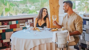 A couple dining at a table with a view of the outdoors, featuring a patterned wall and a wooden pillar. - Hotel Corte Bianca, Bovi's Hotels - Adults Only (Cardedu)