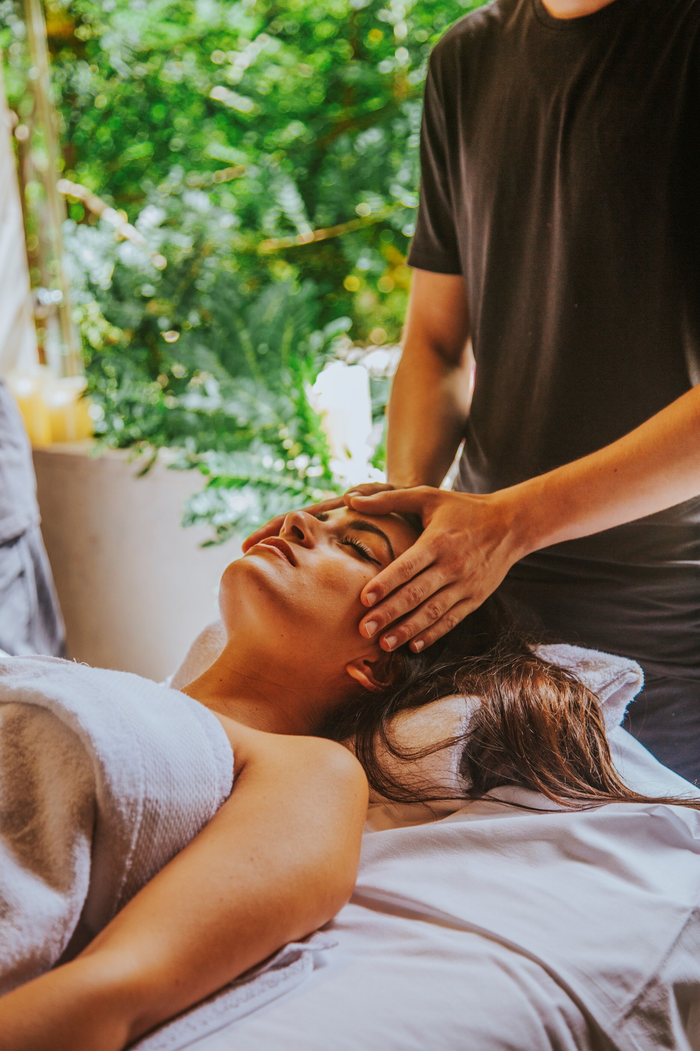 Une personne allongée sur un lit, recevant un massage de la tête.