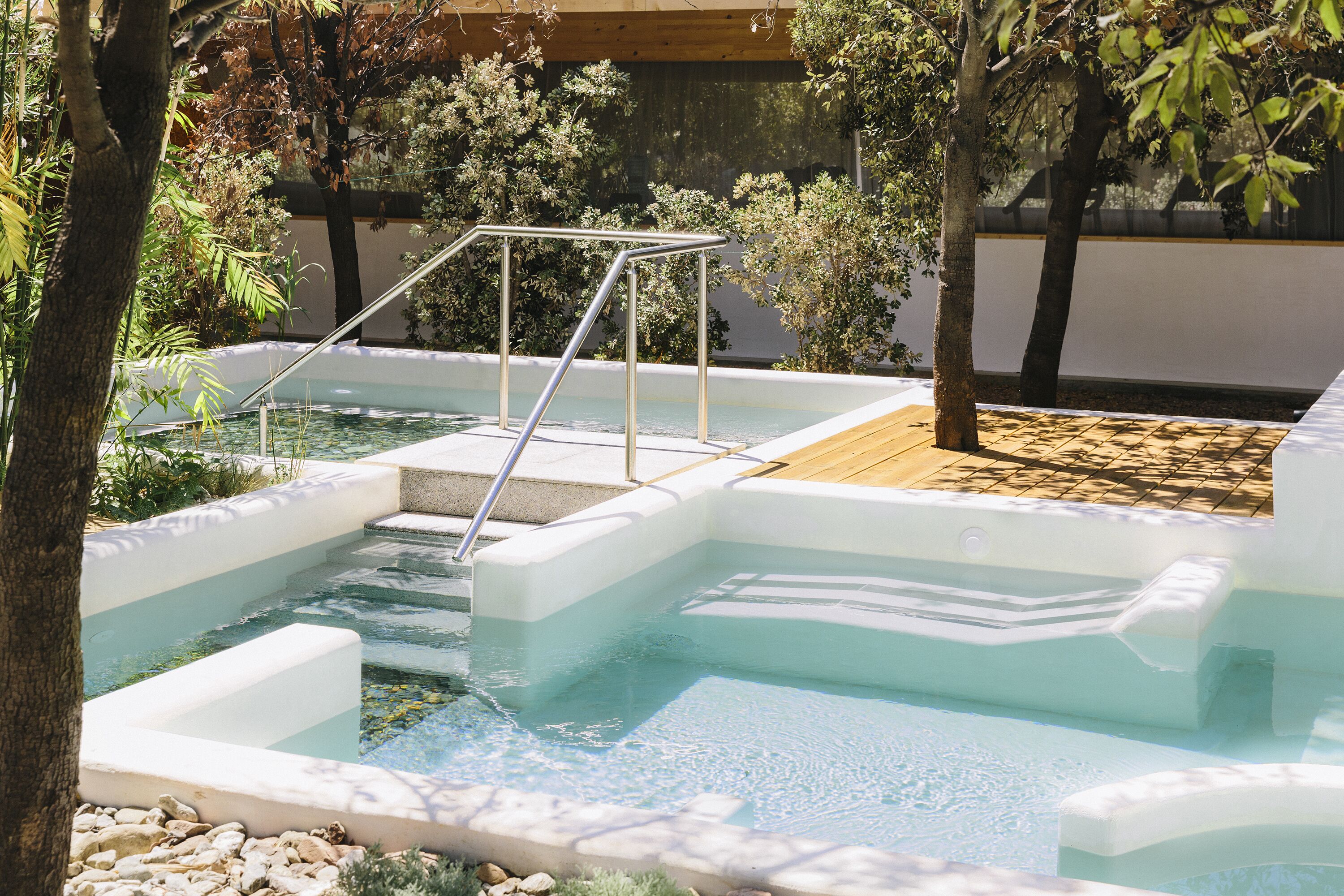 Une piscine avec des marches et une rampe métallique, entourée d’arbres et bordée d’une terrasse en bois.
