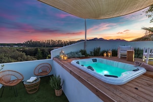 Terraza en la azotea con un jacuzzi, sillas de mimbre y vistas a las montañas al atardecer.