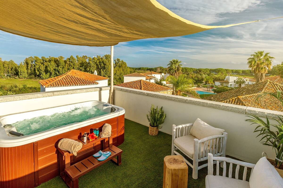 A rooftop terrace with a hot tub, wooden seating, and a view of a village.