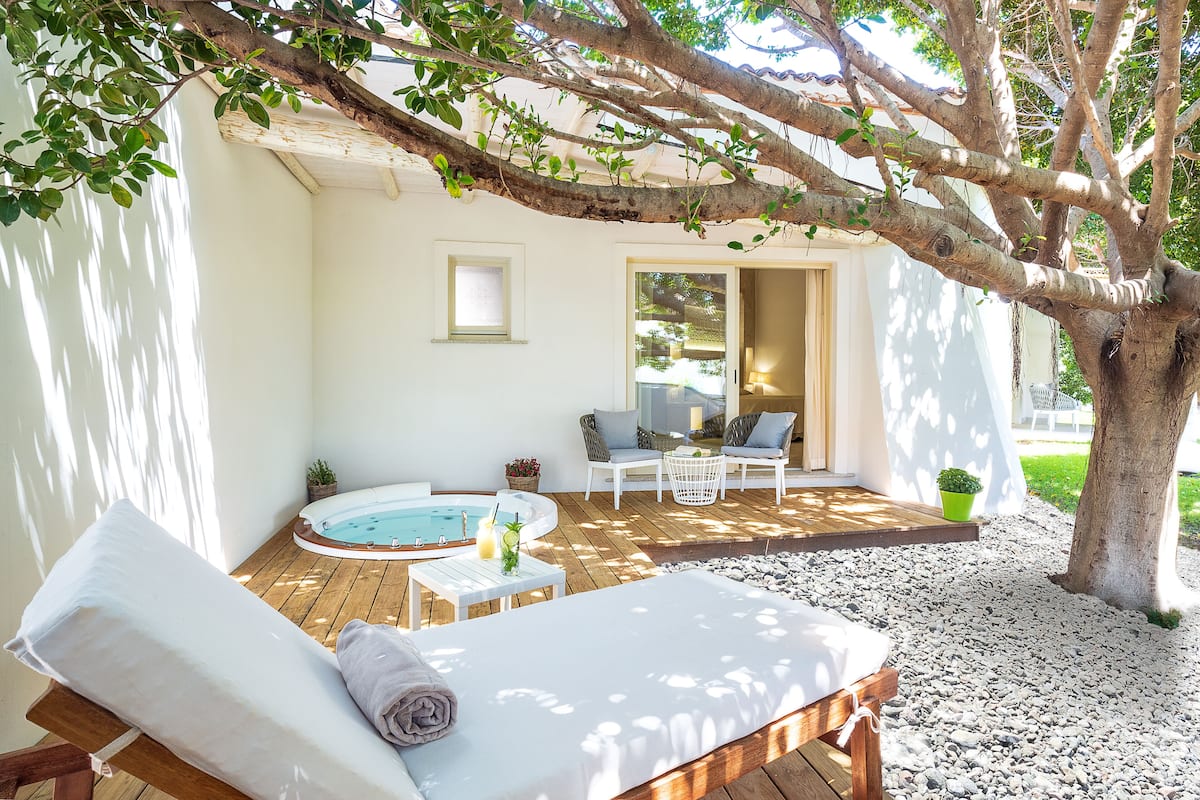 A wooden deck with a hot tub, lounge chairs, and a seating area under a tree.