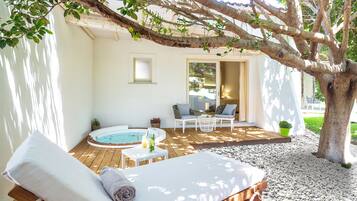 A wooden deck with a hot tub, lounge chairs, and a seating area under a tree.