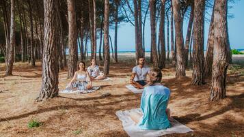 A group of people sitting on mats in a forested area with a beach in the background.