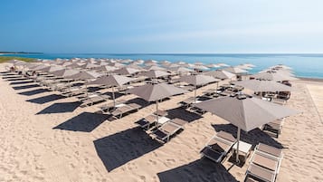Una playa con hileras de tumbonas y sombrillas, un cielo despejado y el océano al fondo.