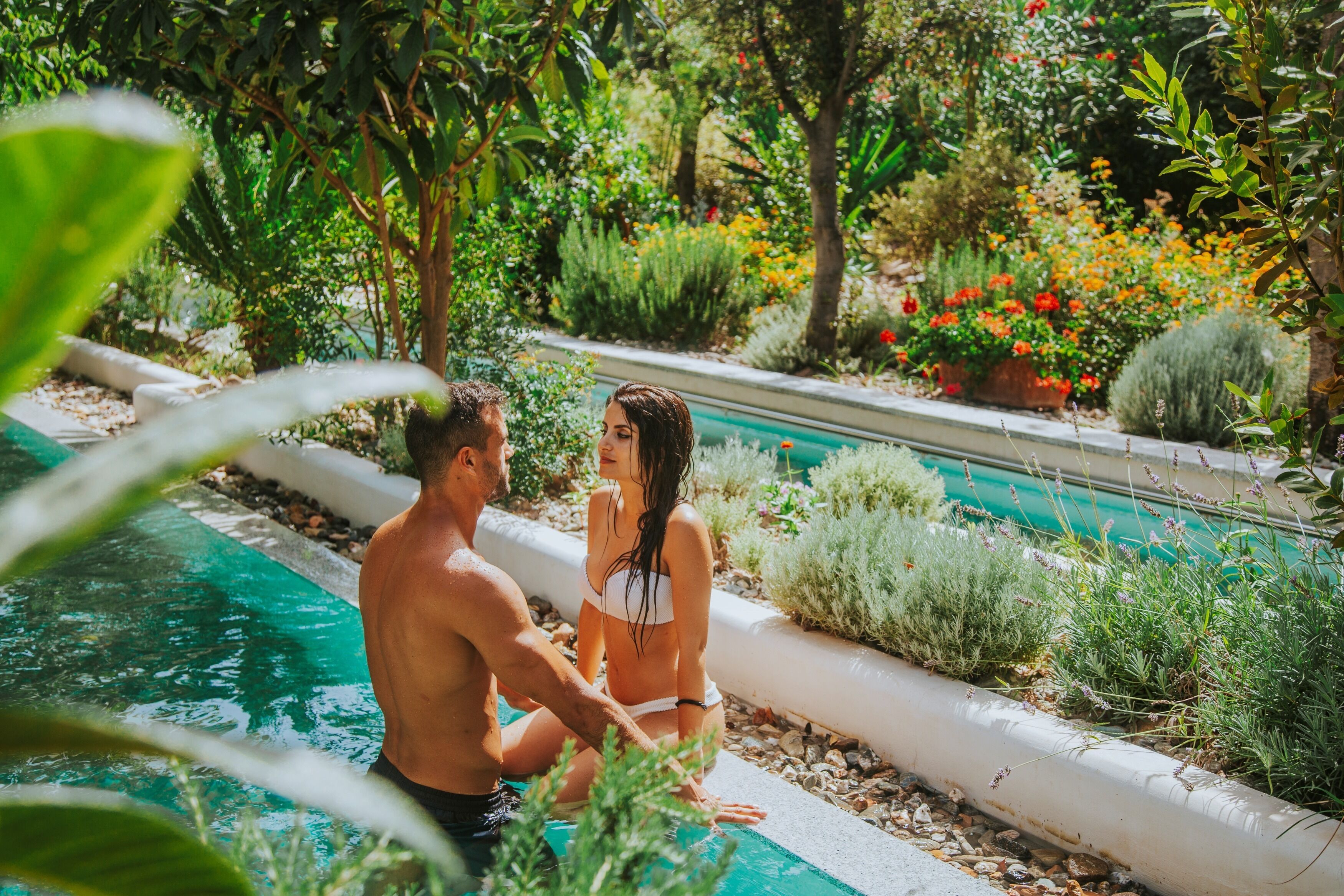 Una coppia accanto a una piscina, sullo sfondo vegetazione lussureggiante e fiori.