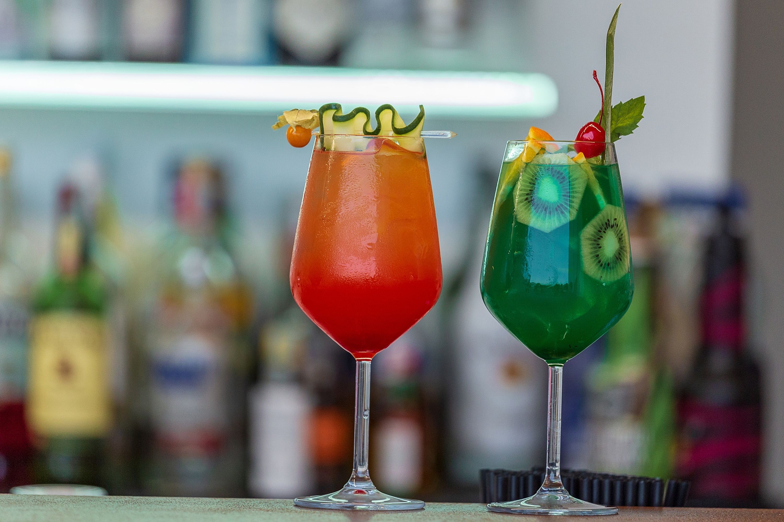 Two cocktails with garnishes on a bar counter.