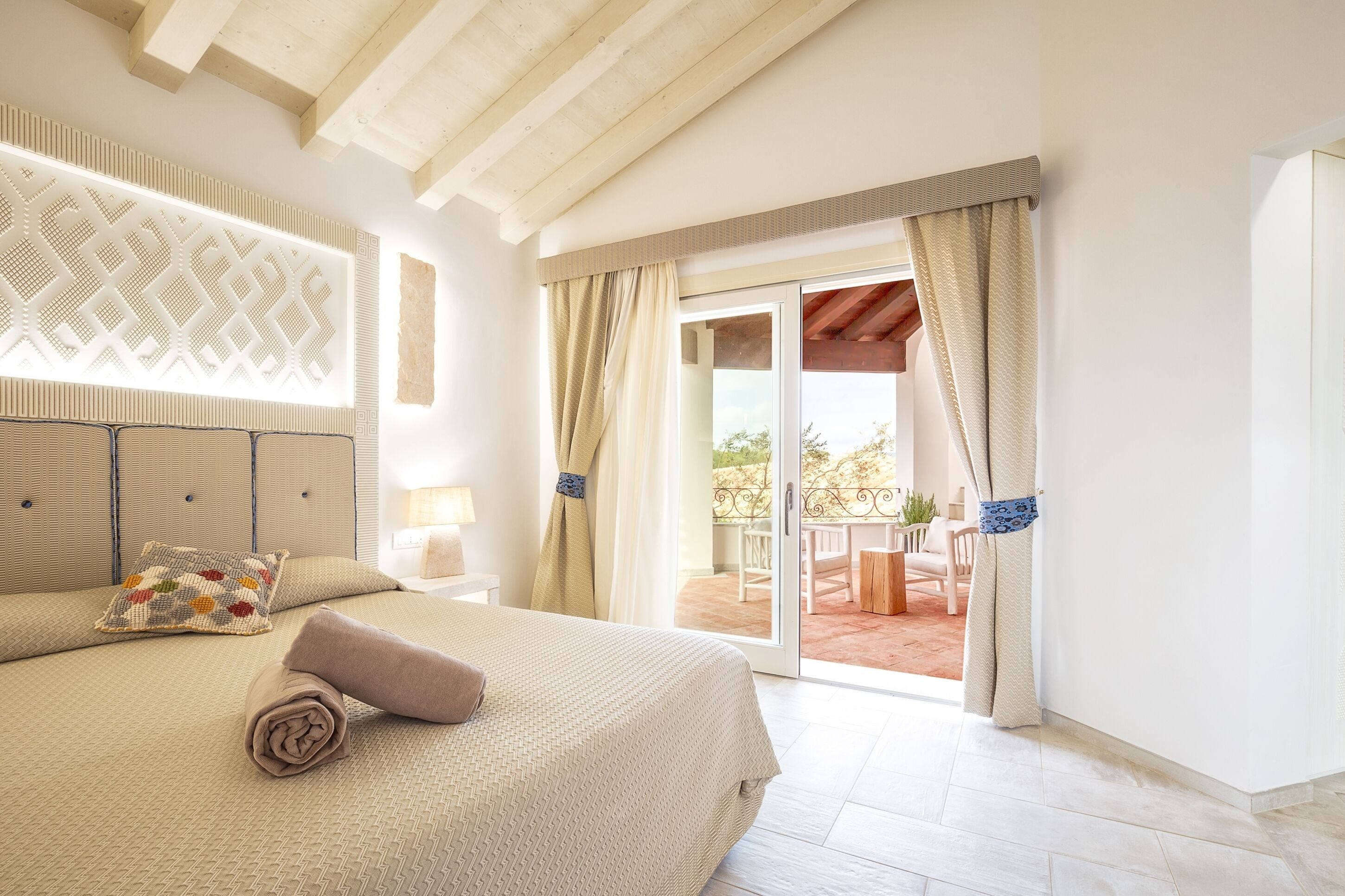 Ein Schlafzimmer mit einem großen Bett, einem dekorativen Kopfteil, Blick auf die Terrasse und einer Schiebetür.