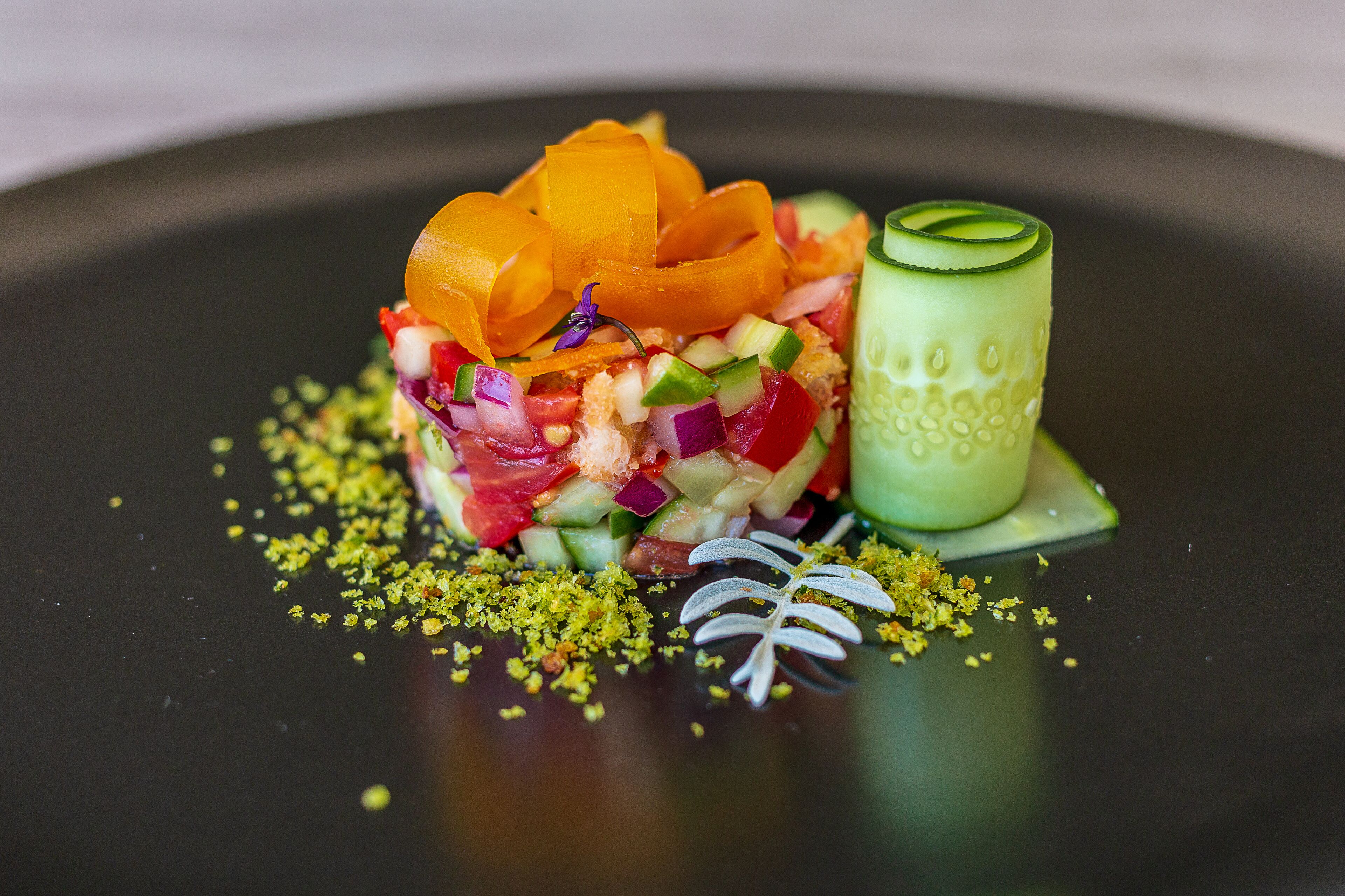 A dish with various colorful ingredients and garnishes on a dark plate.