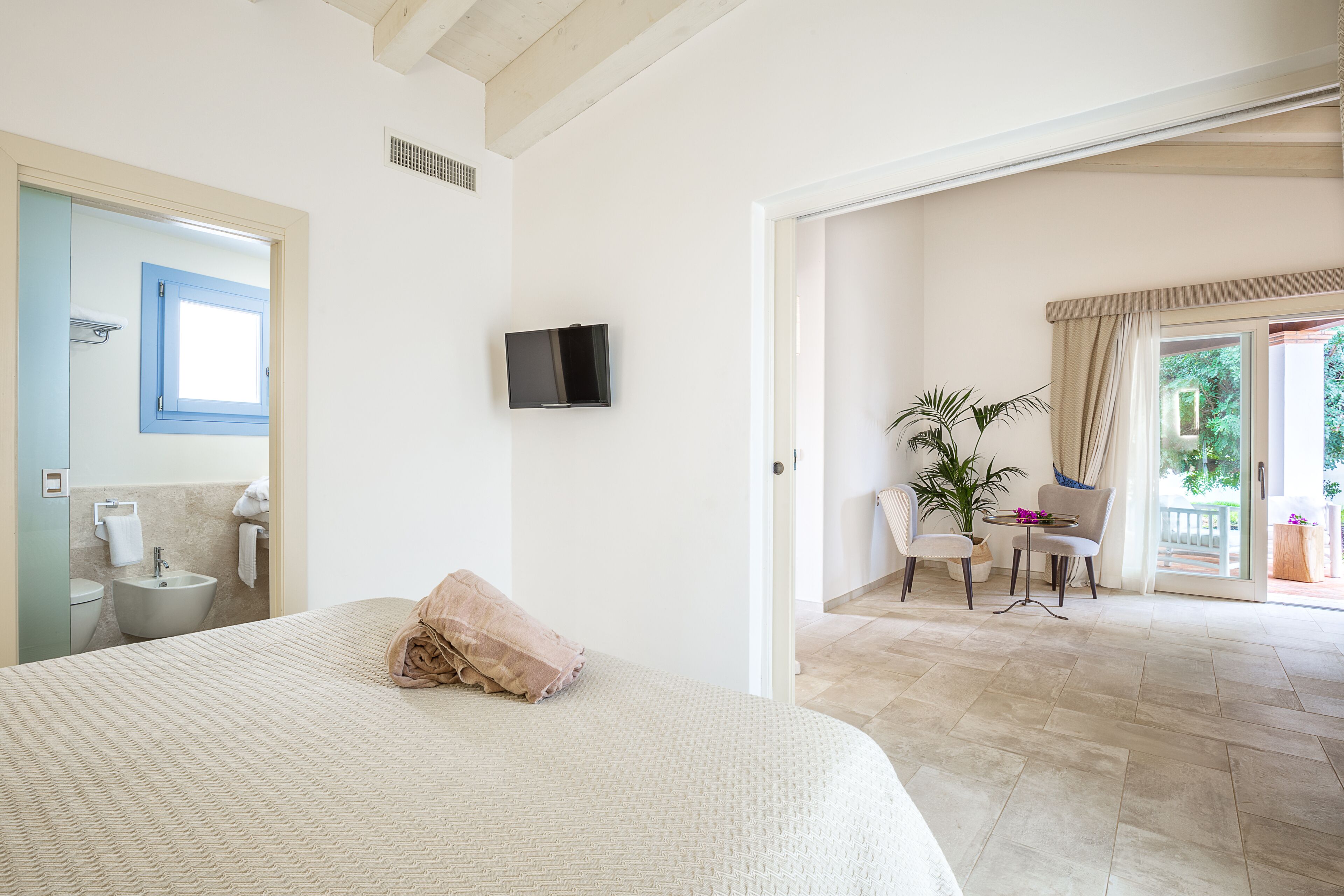 Ein Schlafzimmer mit einem großen Bett, einem an der Wand montierten Fernseher und Blick auf den Balkon.