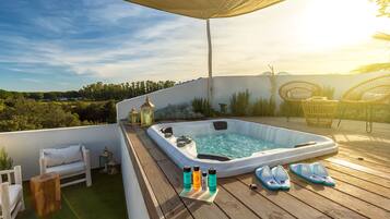 A hot tub on a wooden deck with lounge chairs and a small gazebo.