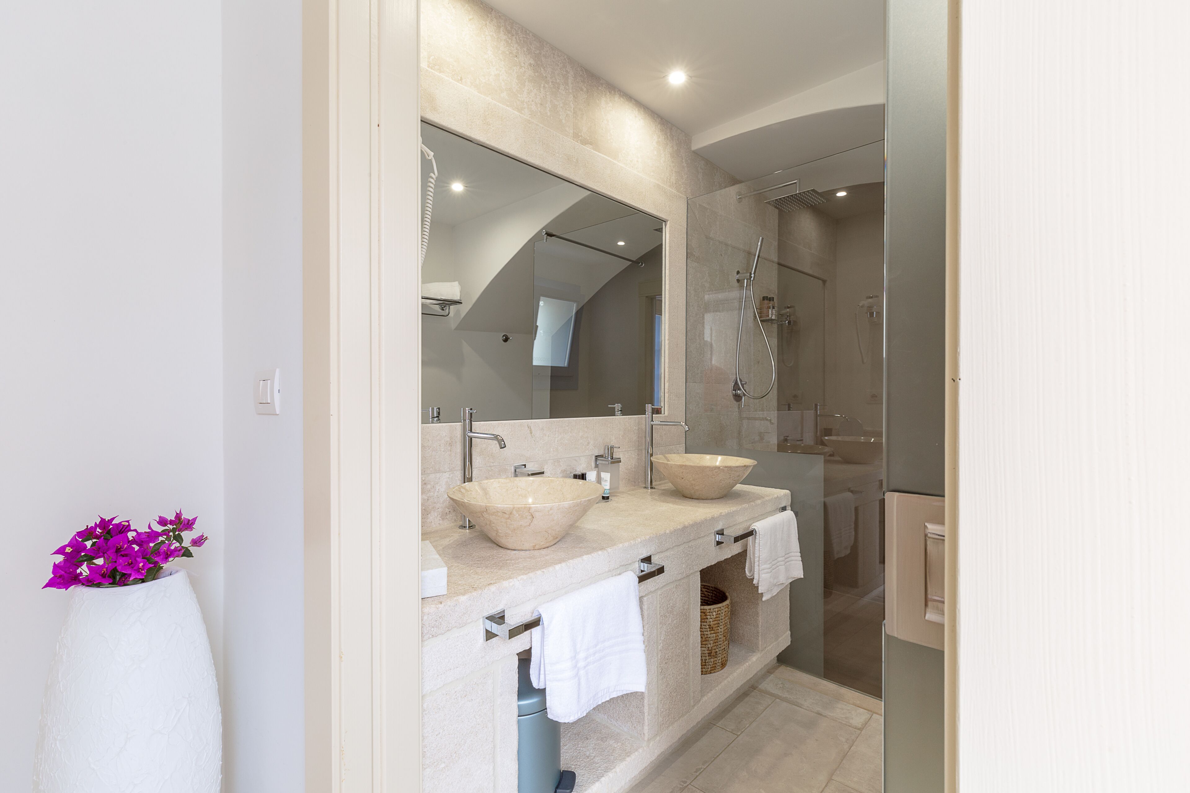 Une salle de bain moderne avec deux grands lavabos de couleur beige, une douche en verre et un grand miroir au-dessus des lavabos.