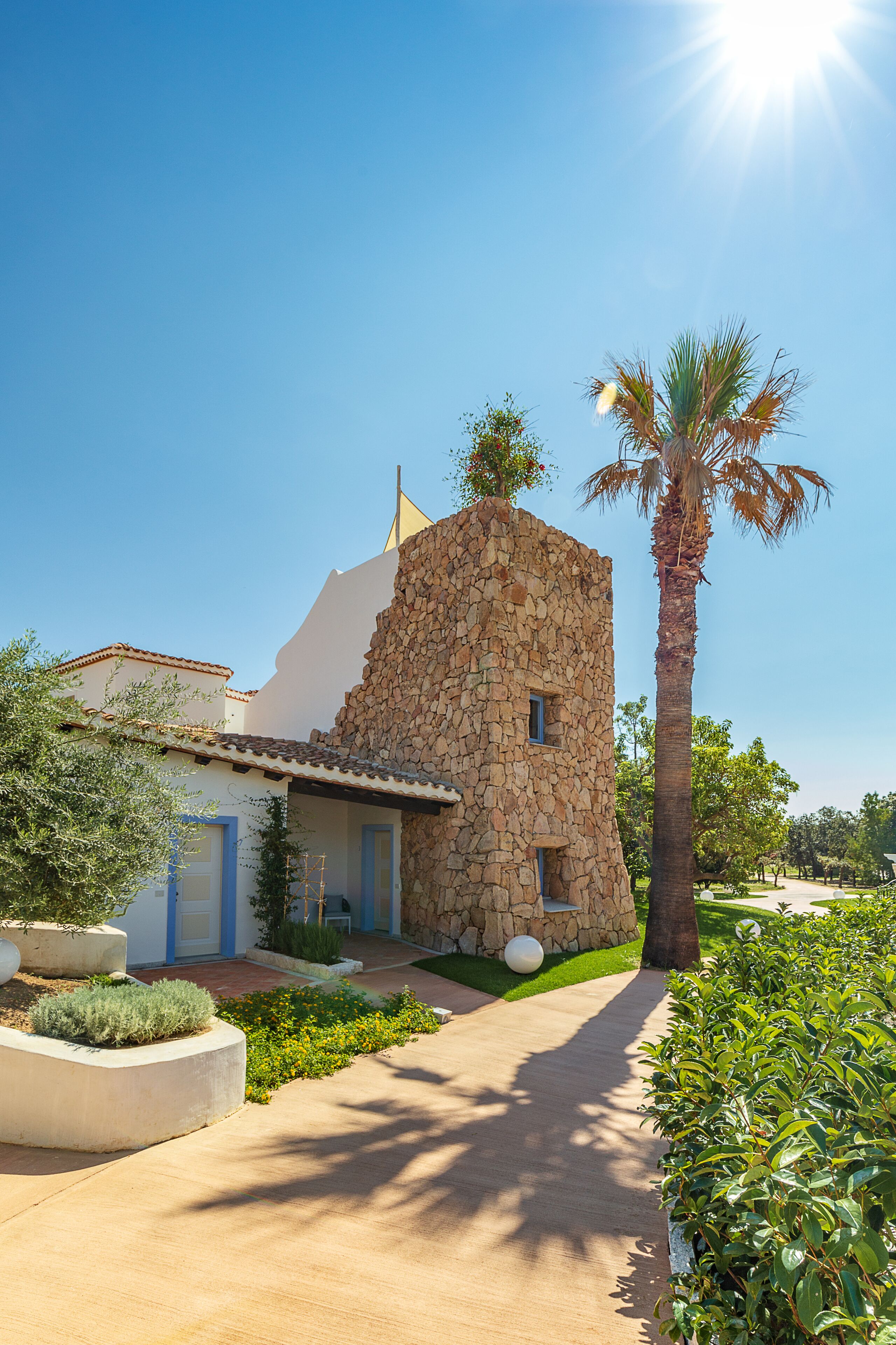 A stone building with a small tower, a palm tree, and a pathway leading to a door.