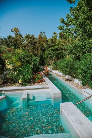 A pool with clear water, surrounded by lush greenery and a stone pathway. - Hotel Corte Bianca, Bovi's Hotels - Adults Only (Cardedu)