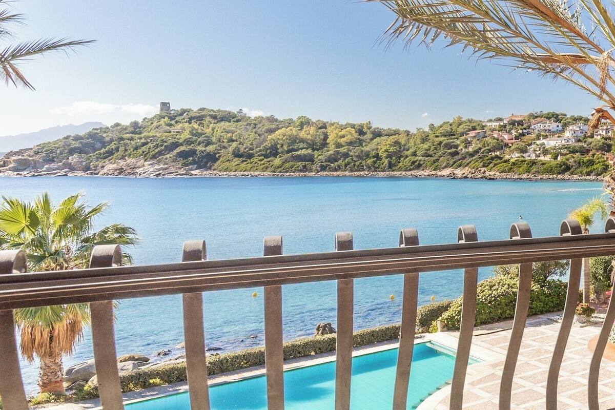 Une piscine offrant une vue sur une zone côtière, notamment une plage et une colline avec des bâtiments.