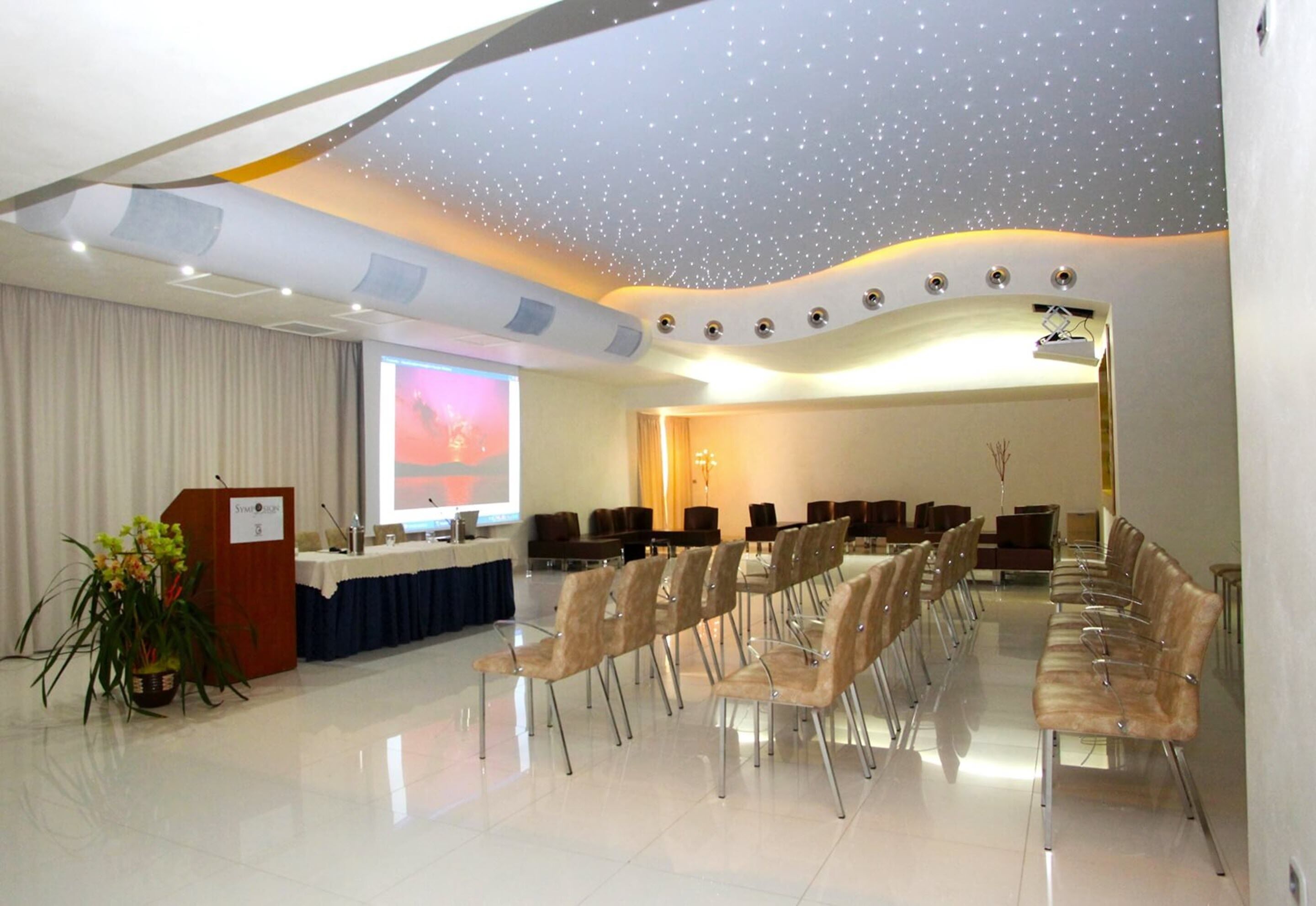 A conference room with a long table, chairs, a podium, and a projector screen.