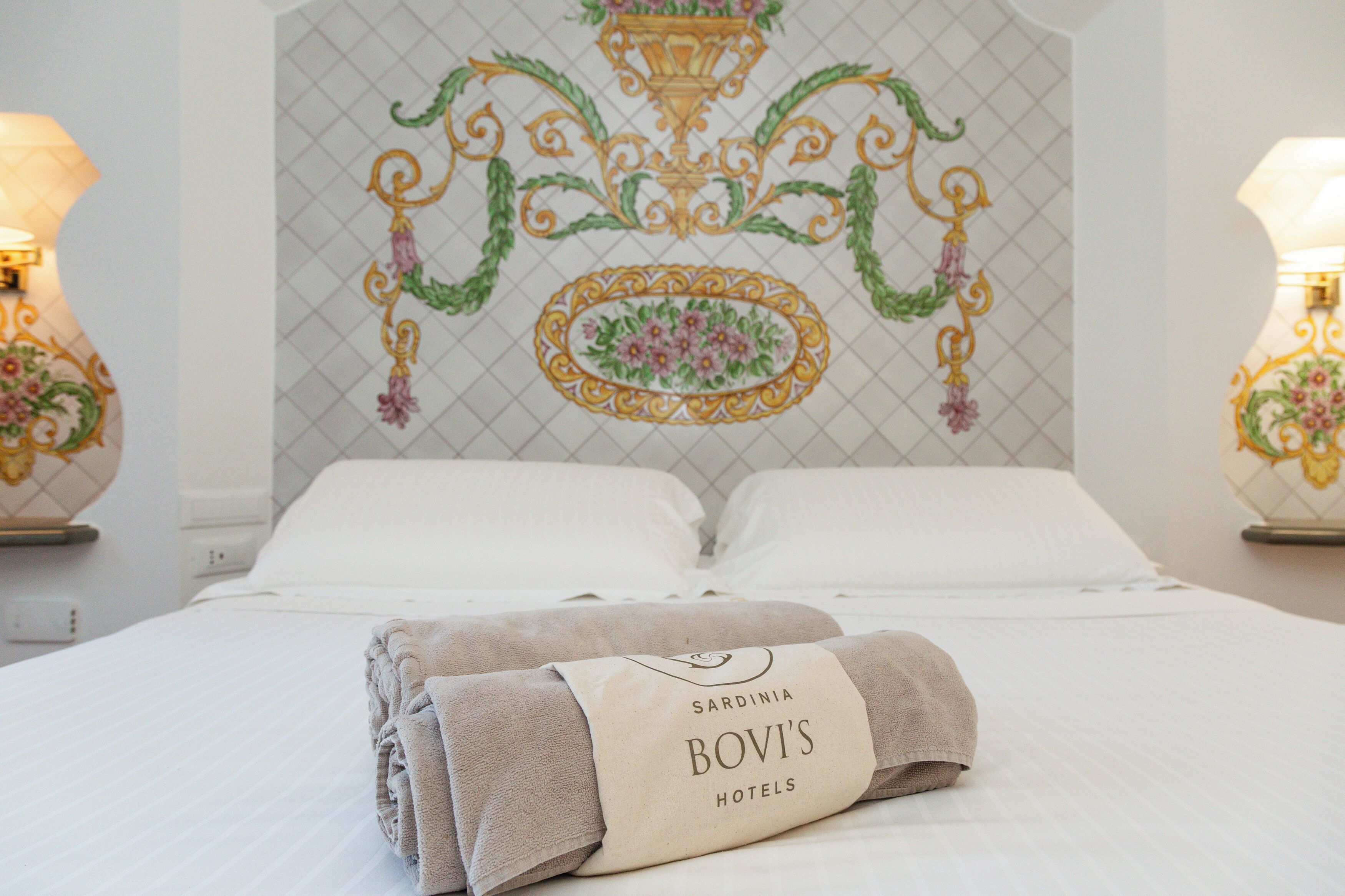 A neatly made bed with a folded towel and a tag reading "Sardinia Bovi's Hotels".
