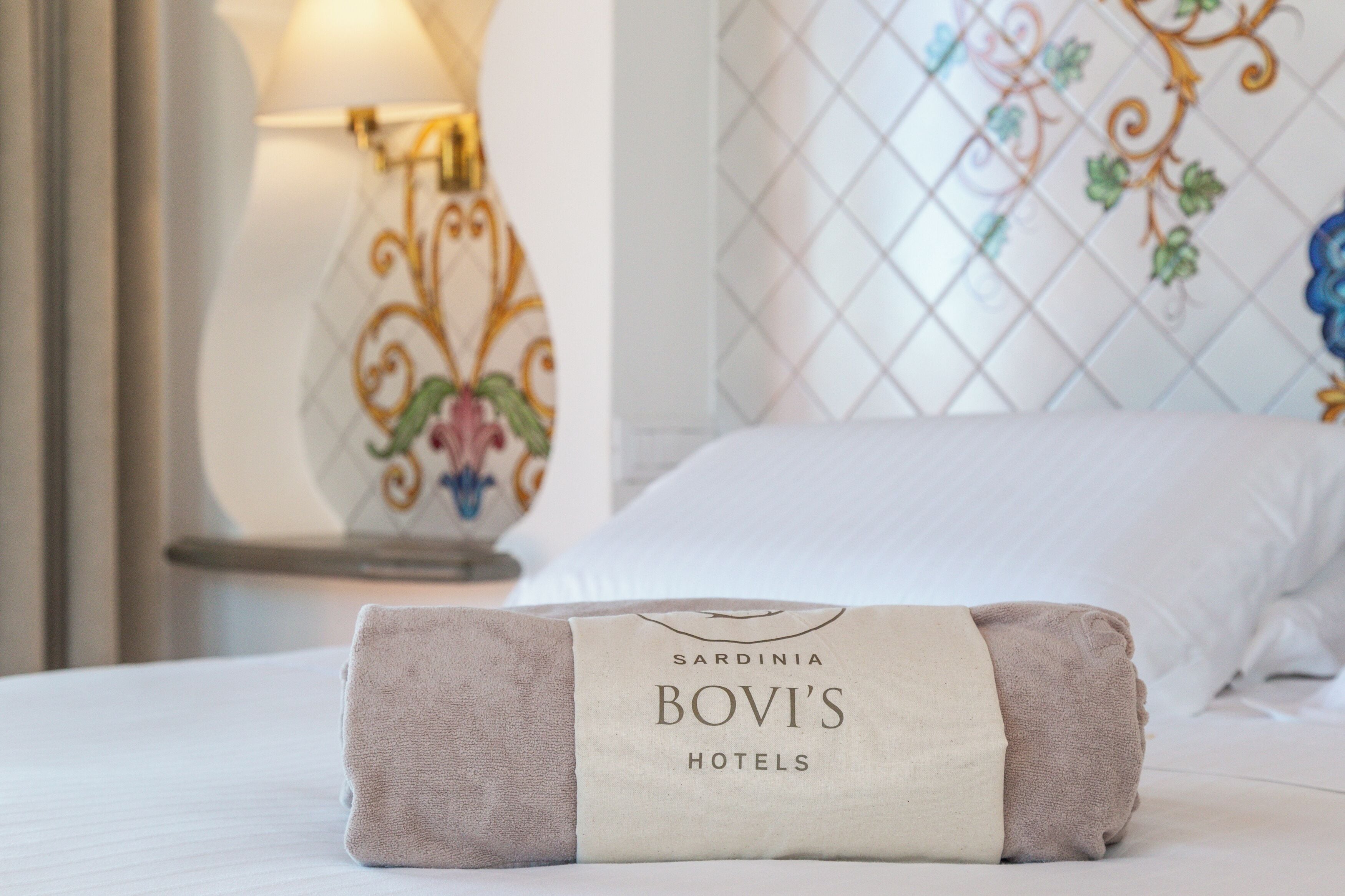 A neatly made bed with a towel and a tag reading "Sardinia Bovi's Hotels".