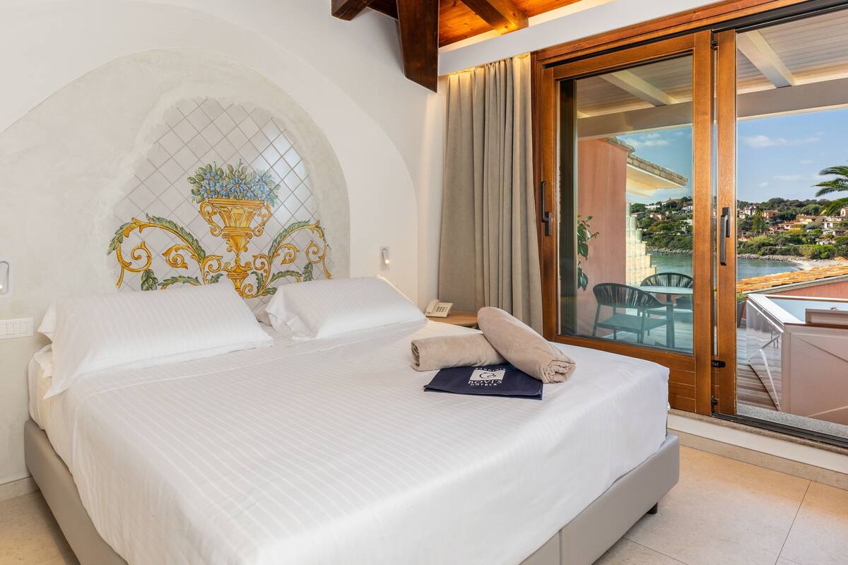 Une chambre d’hôtel avec un lit, une vue sur la mer et un balcon équipé d’une table et de chaises.