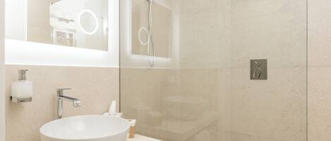 A modern bathroom with a large white sink, a mirror, and a glass-enclosed shower.