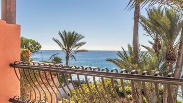 Ein Balkon mit schmiedeeisernem Geländer, der auf eine Küstenlandschaft mit Palmen und Meer blickt.