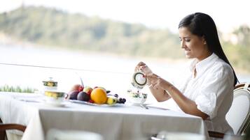 A dining table with a white tablecloth, a teapot, cups, and a variety of fruits.
