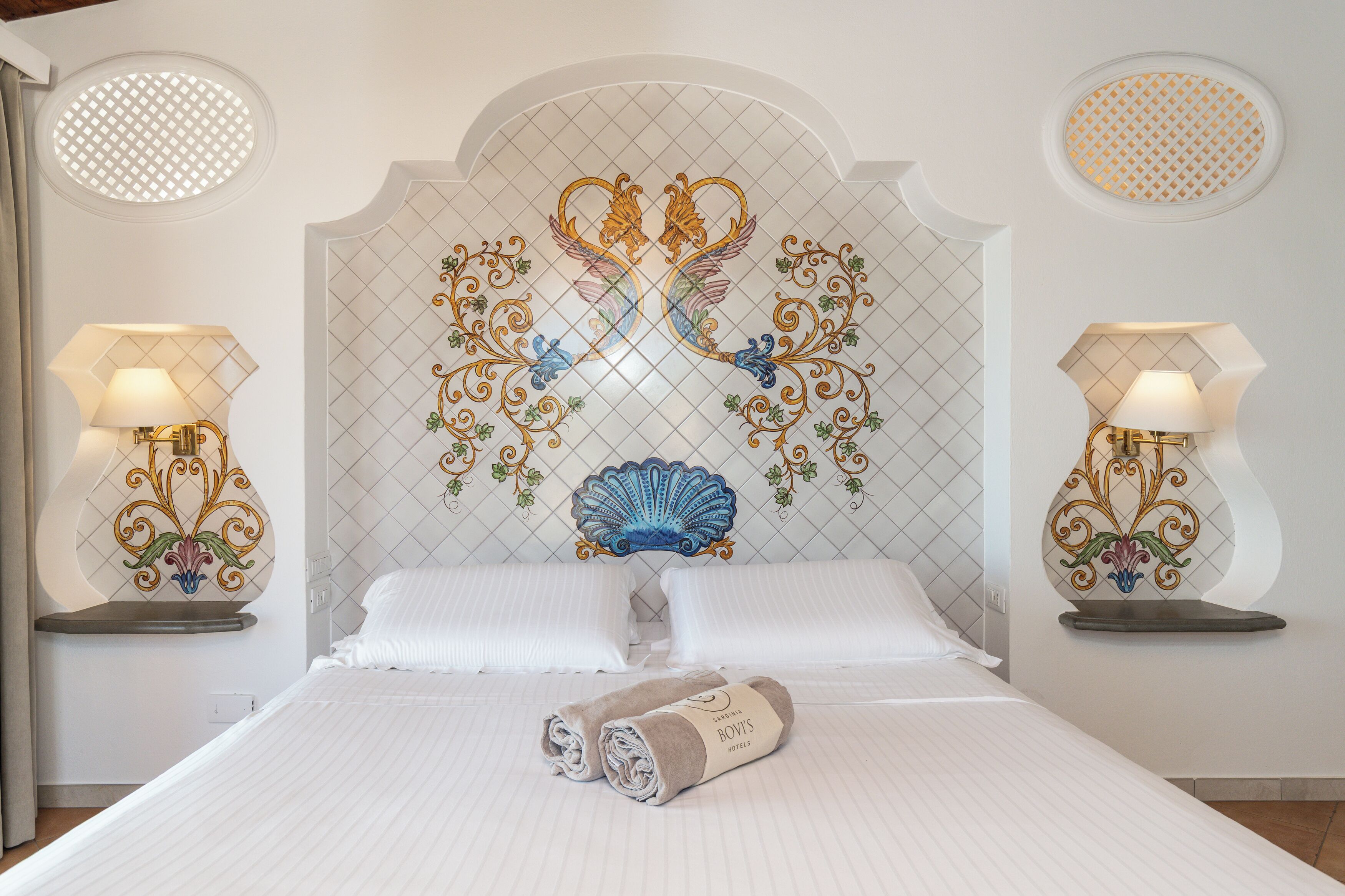Una habitació d'hotel amb un llit gran, dues taules de nit amb làmpades i un panell decoratiu a la paret.