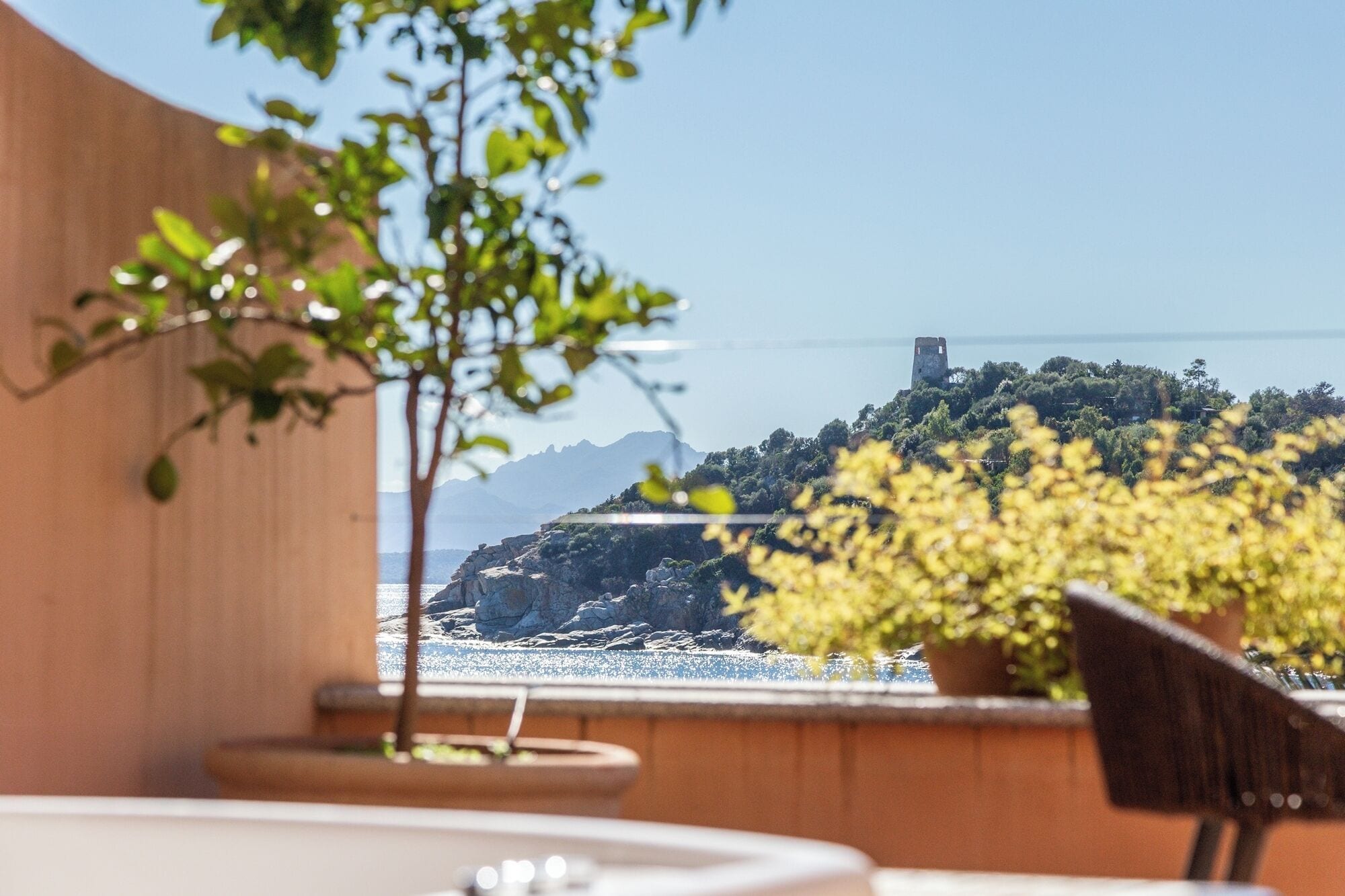 Una terrazza con vista su un paesaggio costiero, che include un promontorio roccioso e una torre.