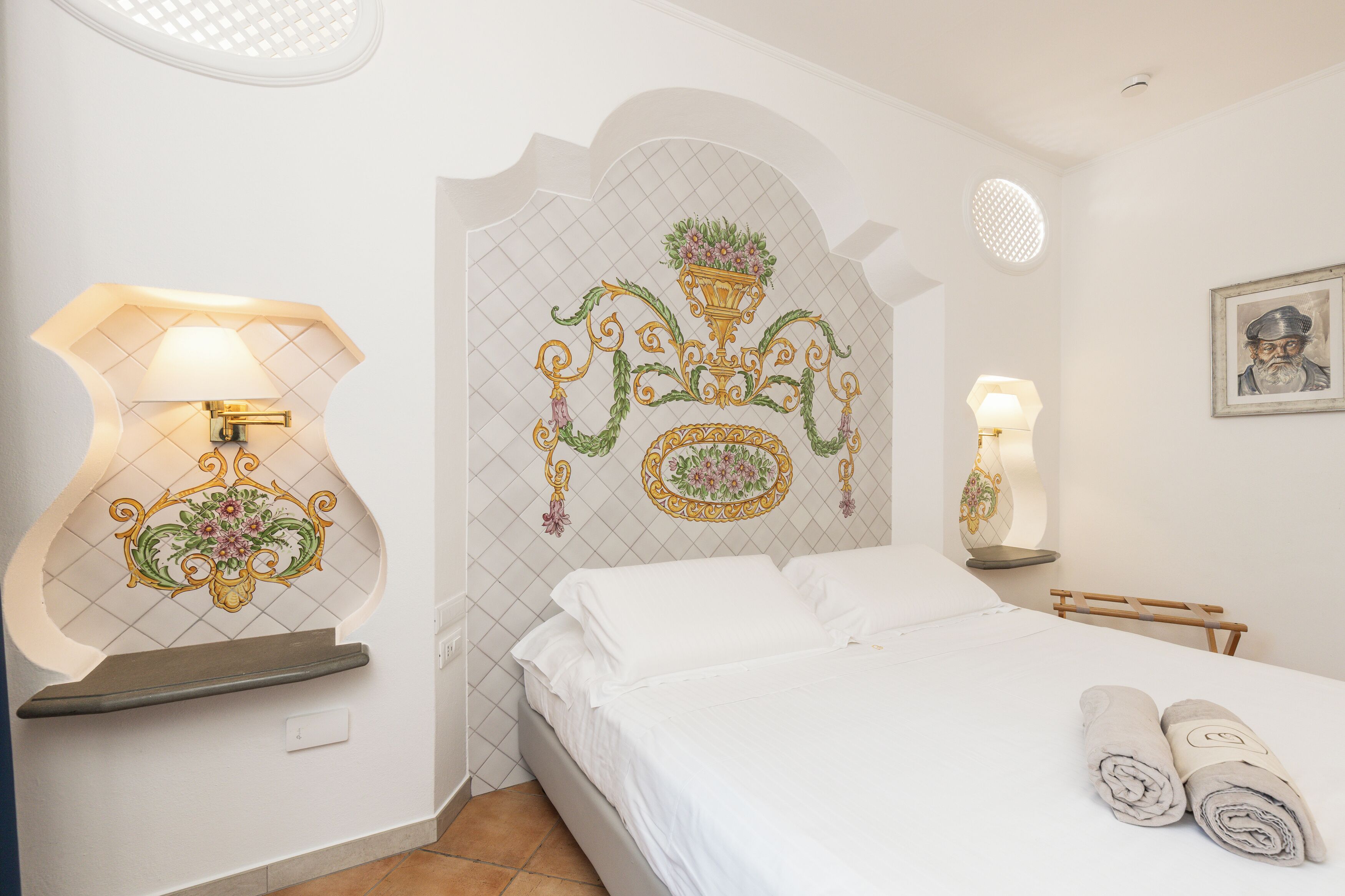 Una camera d'albergo con un letto, un comodino con una lampada, piastrelle decorative e un quadro appeso al muro.