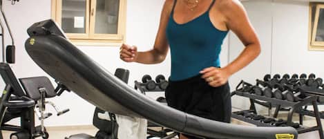 A woman running on a treadmill in a gym with various exercise equipment in the background.