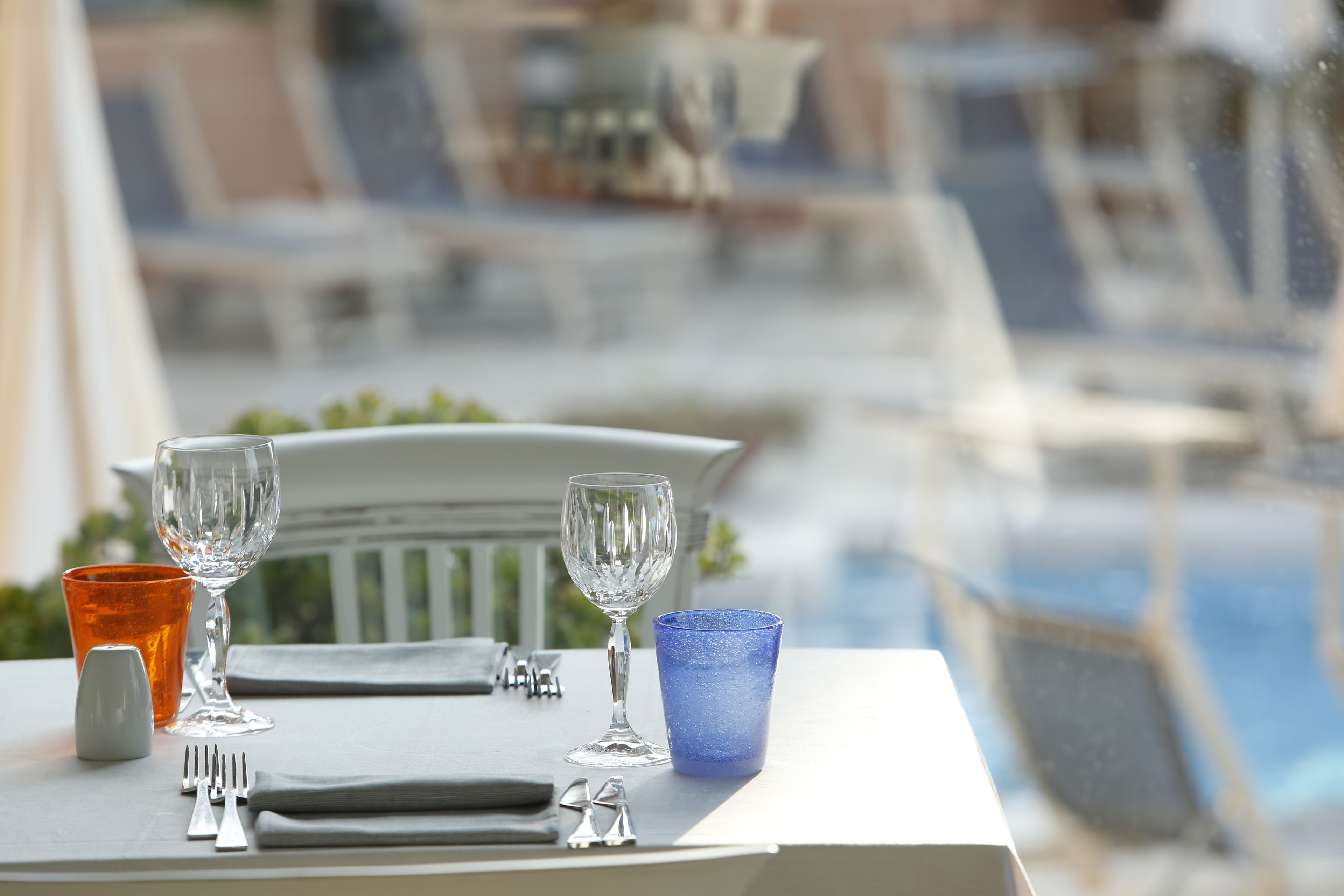 Una tavola apparecchiata con un bicchiere blu, uno trasparente e uno bianco, posate e un tovagliolo.