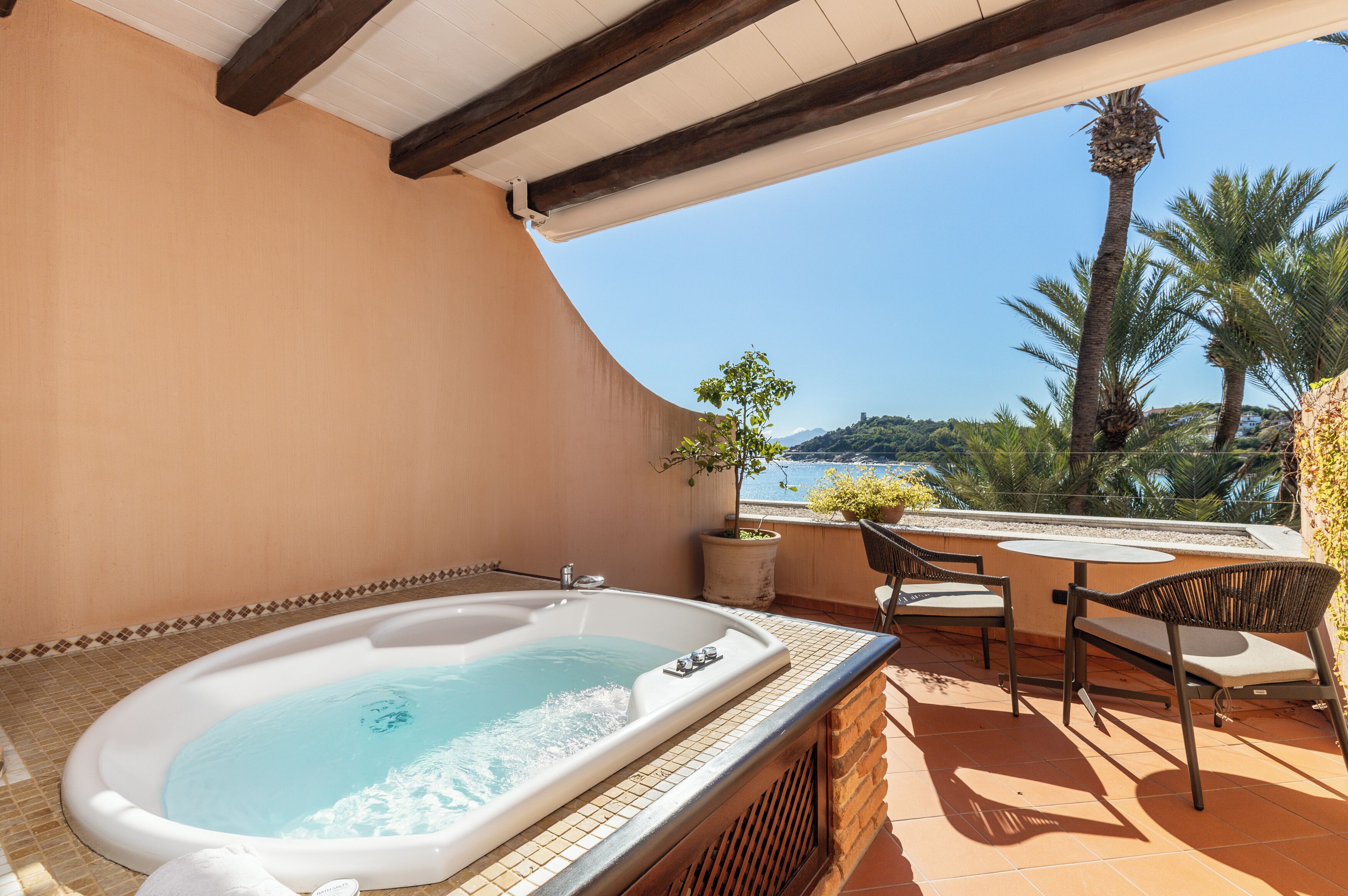 Een bubbelbad op een balkon met uitzicht op zee en palmbomen.