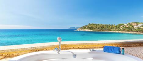 A bathtub with a view of the sea and a tiled area.