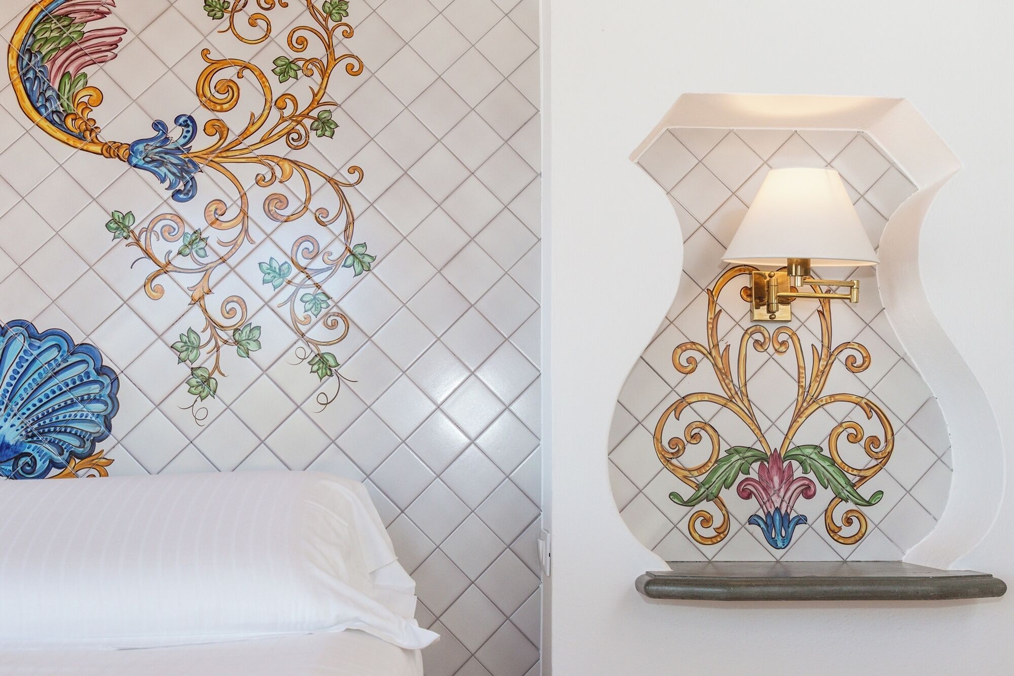 A hotel room with a decorative wall tile design, a bed, and a wall-mounted lamp.