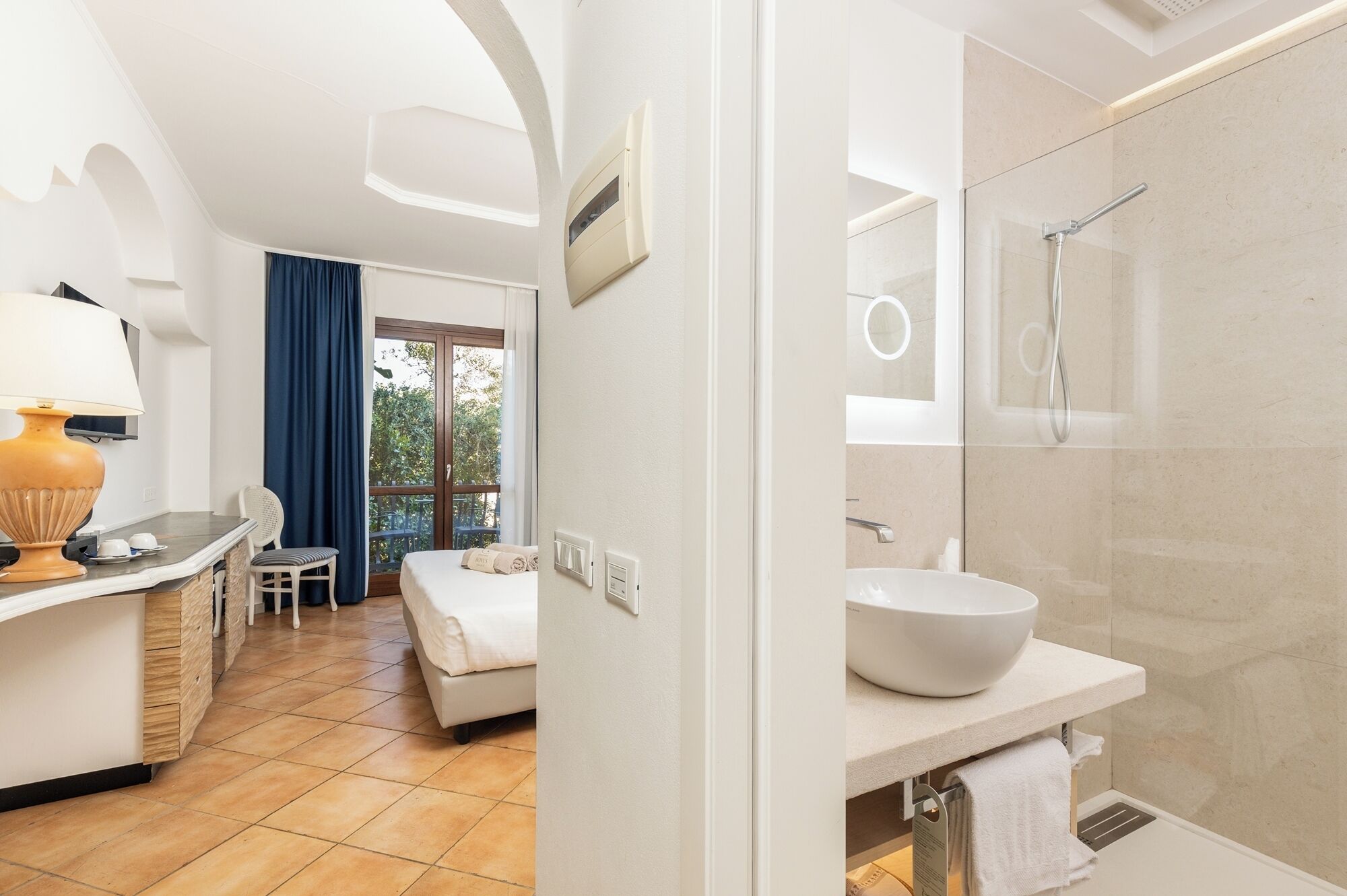 Ein modernes Hotelzimmer mit einem großen Bett, einer Sitzecke mit Tisch und Stühlen, sowie einem Badezimmer mit einem großen Spiegel und einem weißen Waschbecken.