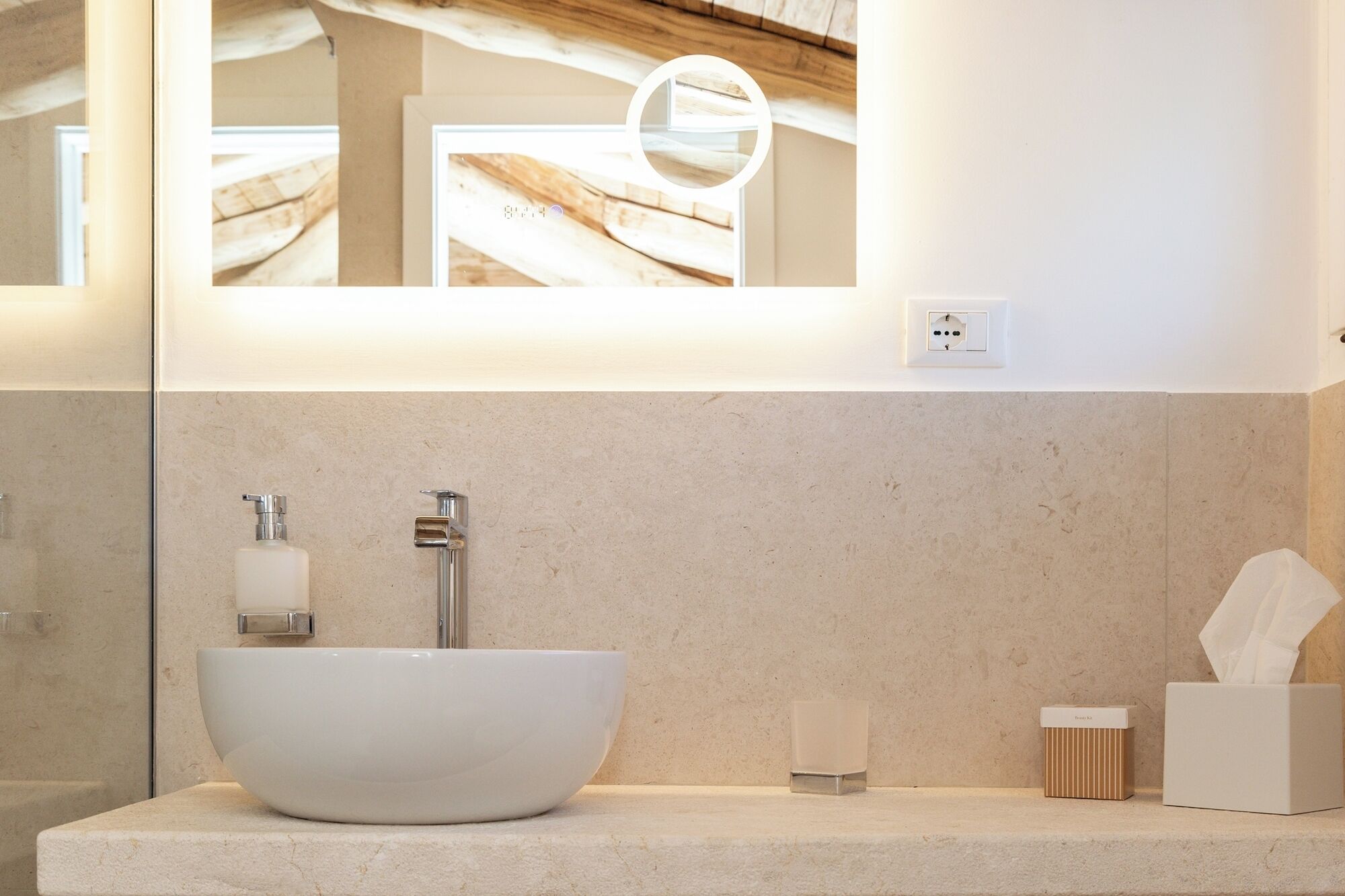 A modern bathroom with a large white vessel sink, a mirror, and a towel dispenser.