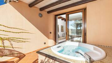 Una vasca idromassaggio con rivestimento in piastrelle, soffitto in legno e una porta scorrevole in vetro che dà su uno spazio esterno.
