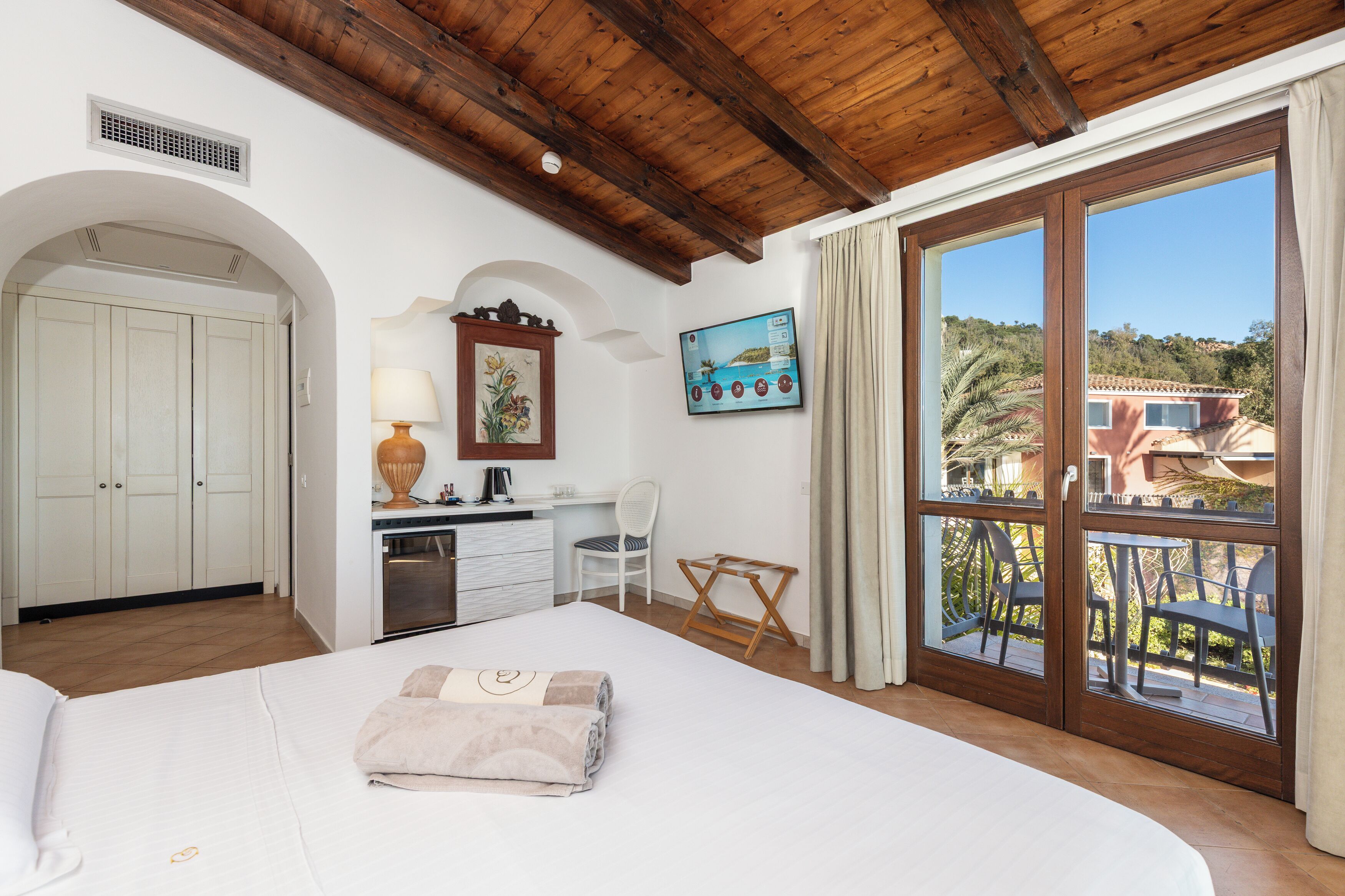 Habitación de hotel con cama, escritorio, silla y balcón con vistas al paisaje.