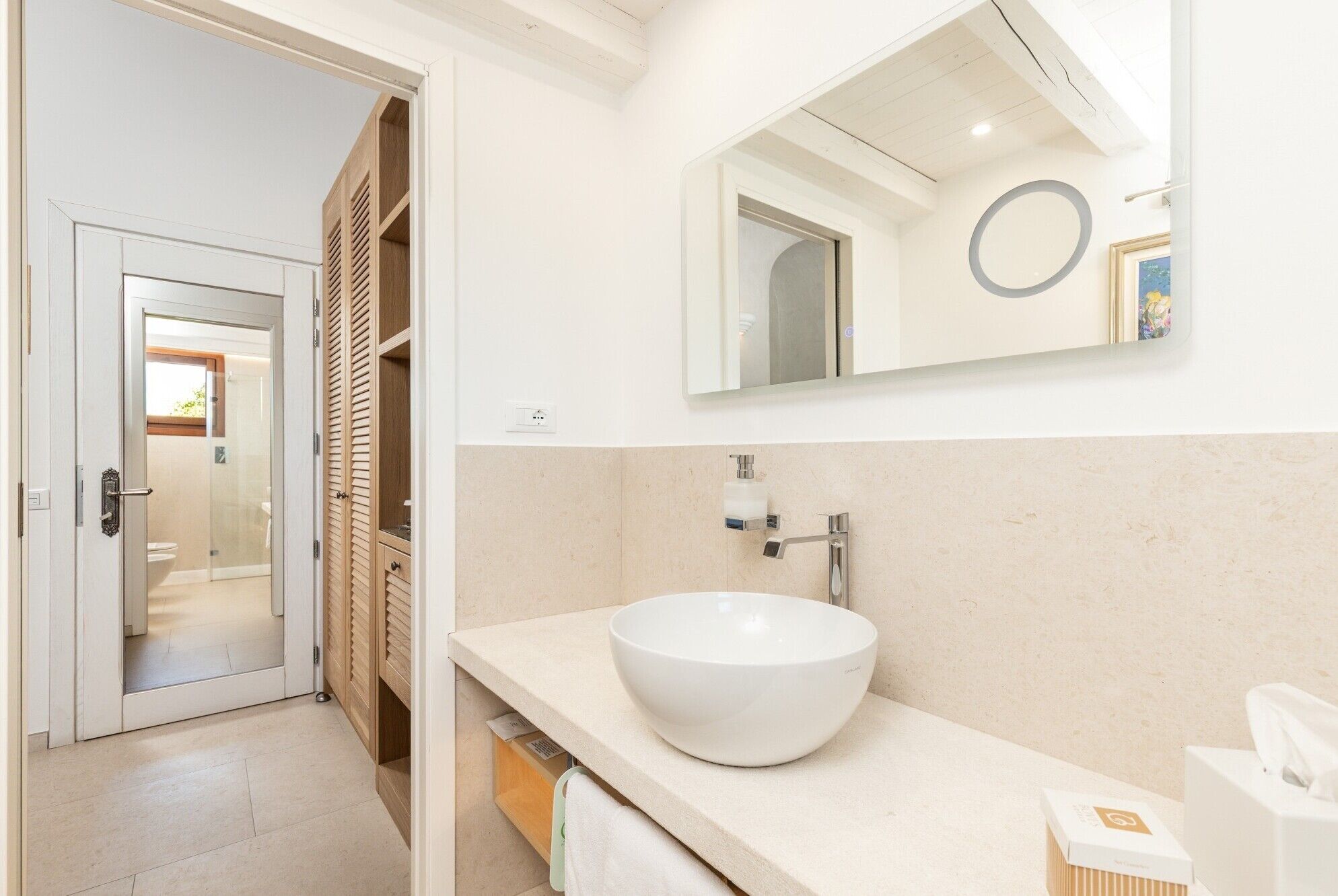 A modern bathroom with a large white sink, a mirror, and a wooden storage unit.