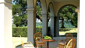 A covered patio area with four wicker chairs and a round table, surrounded by white columns.