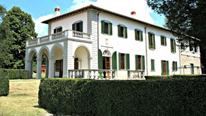 A white building with green shutters, a balcony, and a statue in front.