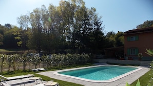 A rectangular swimming pool with a tiled deck, surrounded by a well-maintained lawn and a variety of plants. - Casa Marcoiano (Scarperia e San Piero)