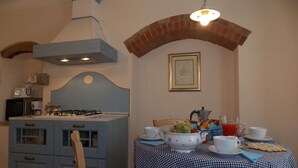 A dining area with a checkered tablecloth, a gas stove, and a brick arch above the table. - Casa Marcoiano (Scarperia e San Piero)