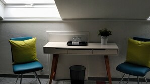 Une petite pièce moderne, dotée d’une lucarne, d’un bureau, de deux chaises, d’une poubelle et d’une plante en pot.