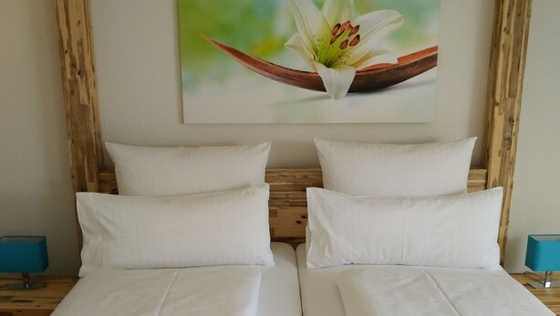 Un lit double avec du linge de lit blanc, une tête de lit en bois et un tableau représentant une fleur accroché au mur.