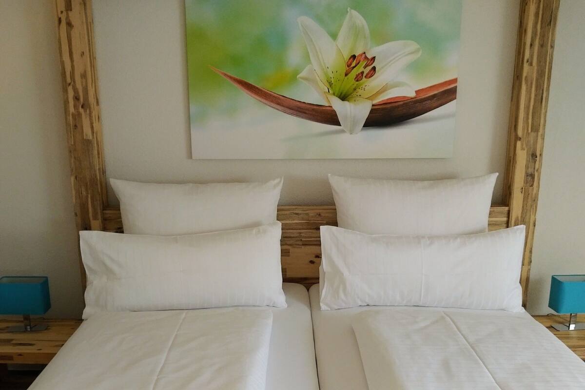 Una cama doble con ropa de cama blanca, un cabecero de madera y un cuadro de una flor en la pared.