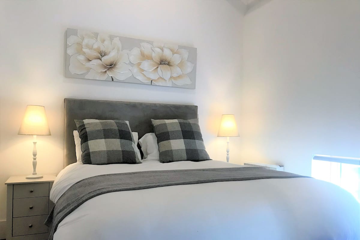 A neatly made bed with a grey headboard, two bedside tables with lamps, and a floral artwork above the bed.