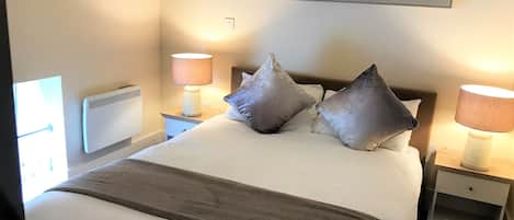 A neatly made bed with pillows, a bedside lamp, and a wall-mounted artwork of dandelions.