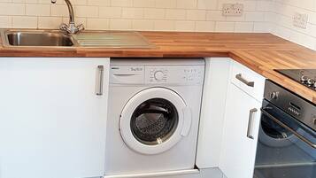 A compact kitchen with white cabinets, a stainless steel sink, a built-in washing machine, and a black oven.