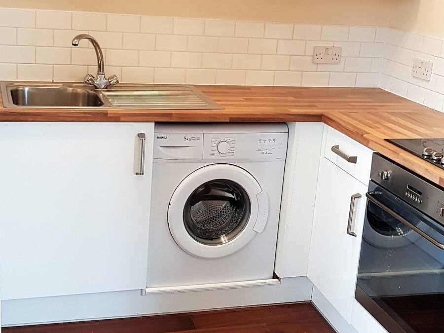 A compact kitchen with white cabinets, a stainless steel sink, a built-in washing machine, and a black oven.
